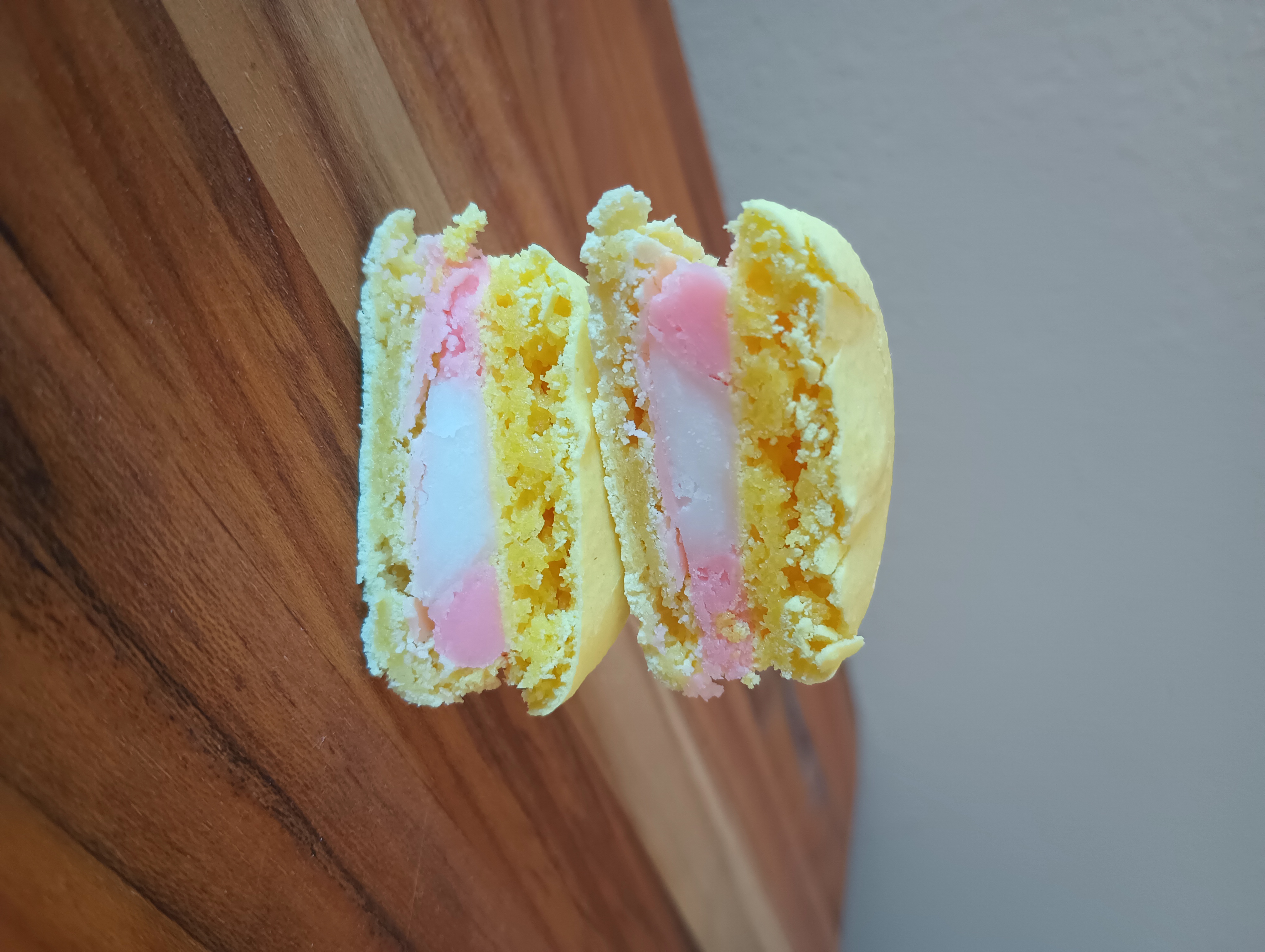 A yellow and pink raspberry lemonade macaron cut in half to show the fillings